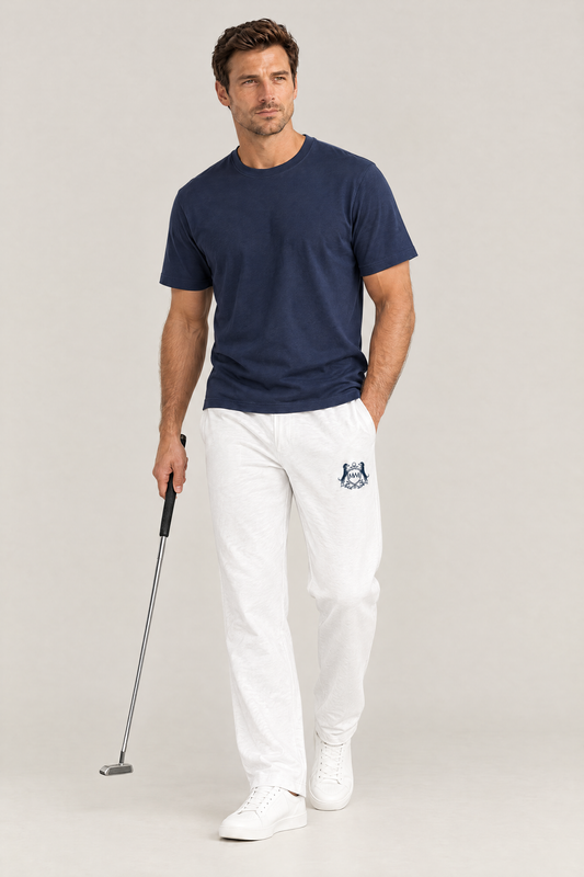 Man walking with a putter in white straight-leg Club Crest sweatpants with the small navy crest on the thigh and a navy tee
