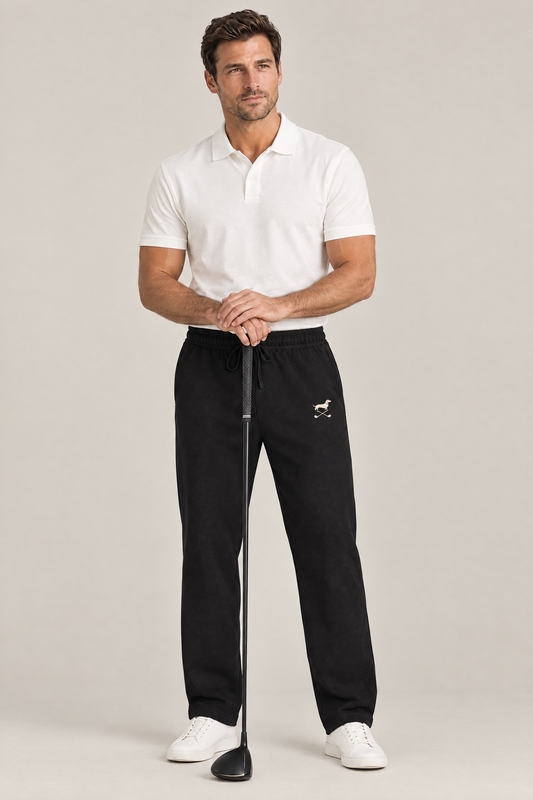 Man resting both hands on a golf driver in black Club Mark dachshund golf sweatpants with the small cream logo on the thigh and a white polo. Color: Black