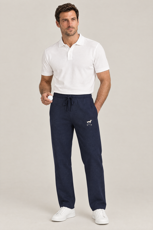 Man holding a golf ball in navy blue Club Mark dachshund golf sweatpants with the small cream logo on the thigh and a white polo. Color: Navy Blue