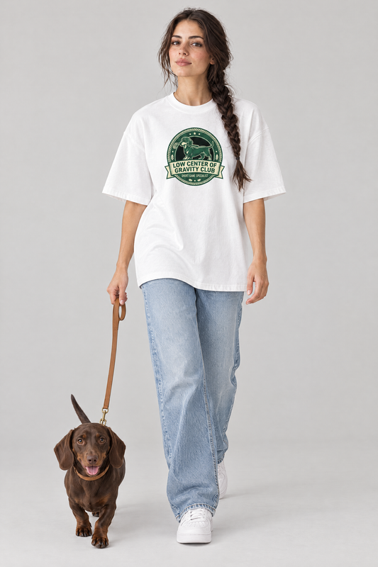 Woman walking a dachshund on a leash in the white Low Center of Gravity Club Dachshund Golf Tee. Color: White