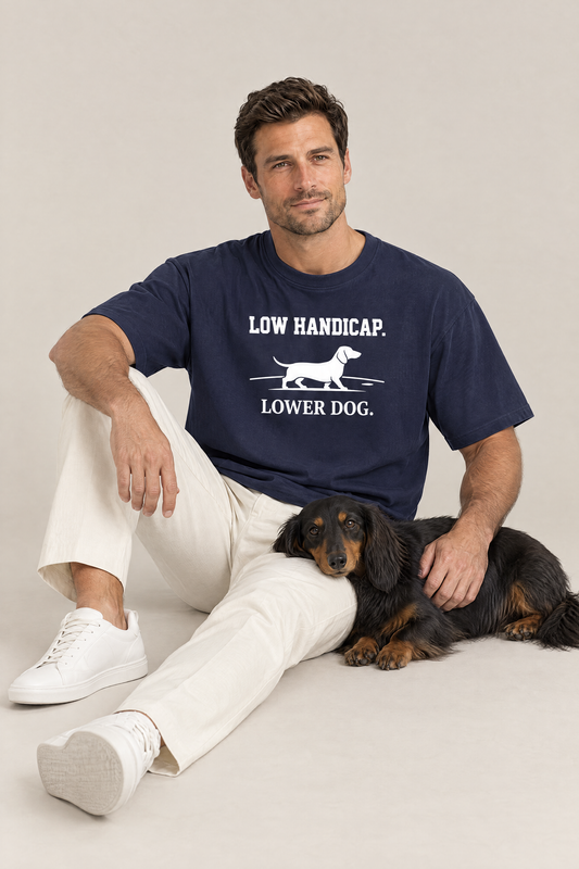 Man sitting on the floor with a long-haired dachshund in the navy Low Handicap Dachshund Golf Tee. Color: Navy