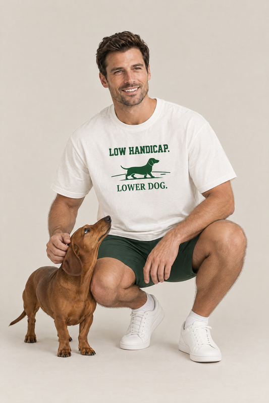 Man crouching next to a red dachshund in the white Low Handicap Dachshund Golf Tee. Color: White