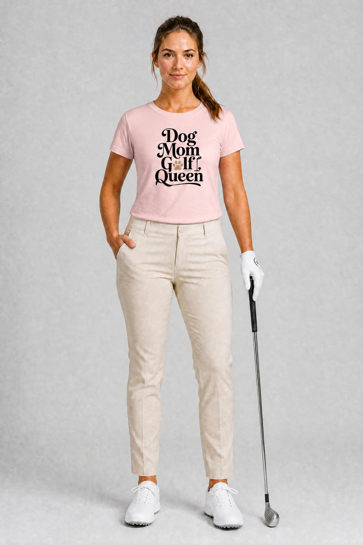 Woman wearing a pink t-shirt with 'Dog Mom Golf Queen' text, holding a golf club on a gray background