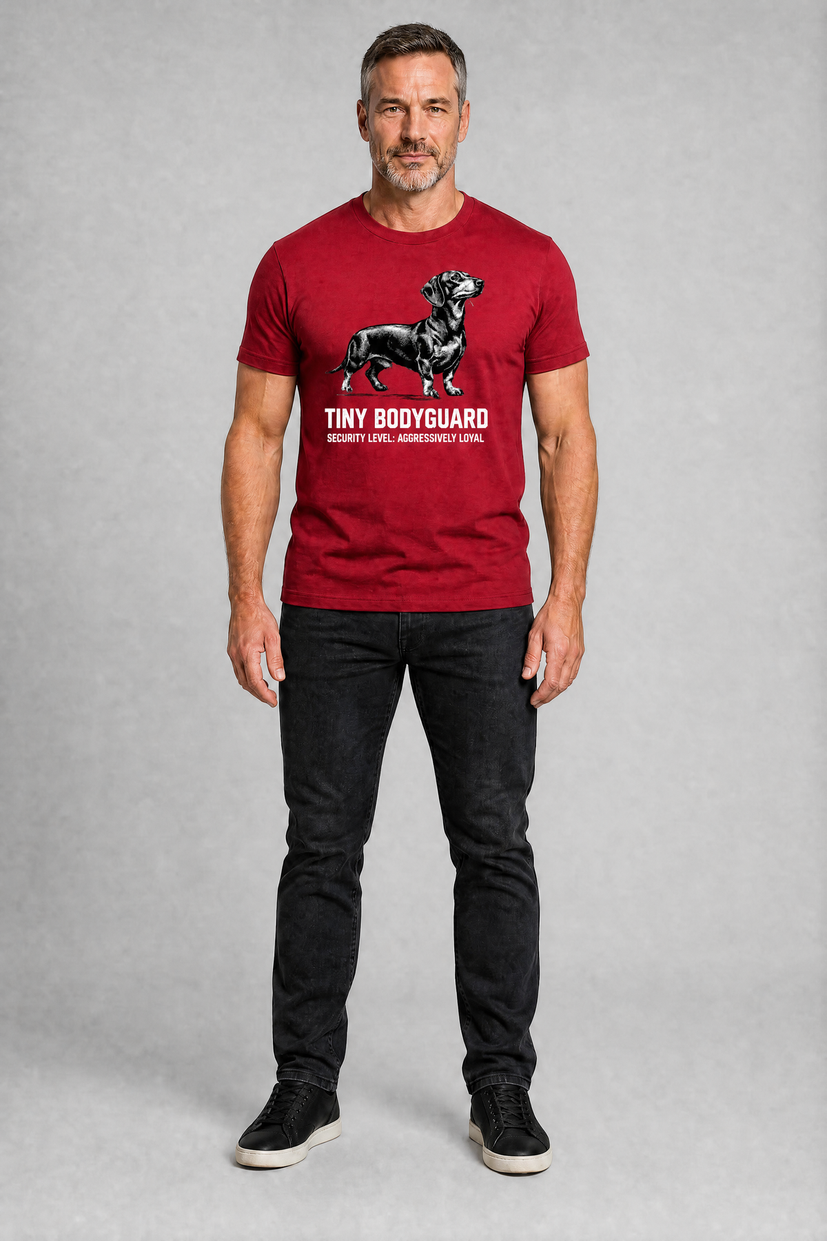 Man wearing a red t-shirt with a graphic and text, standing against a gray background
