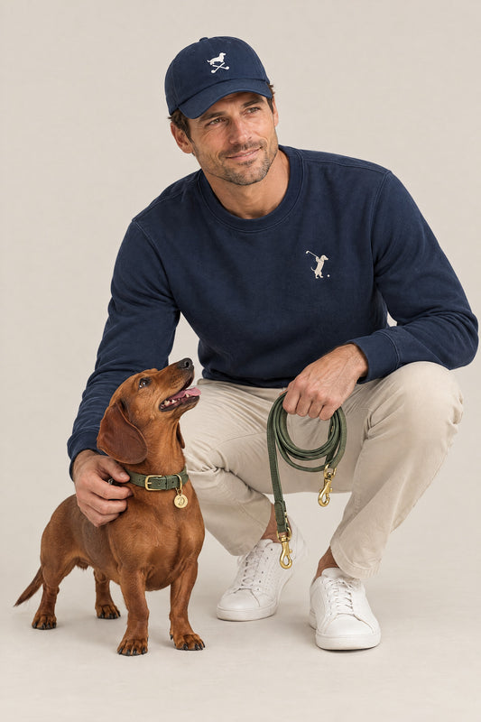 Man in the navy Swing Dachshund golf sweatshirt and cap crouching next to a red dachshund wearing the Cloud 7 Tiergarten Moss collar