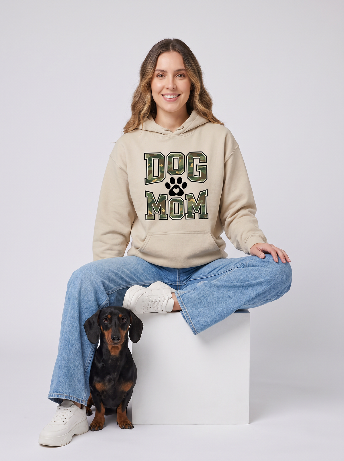 Woman wearing the Camo Dog Mom hoodie in sand with her dachshund. Color: Sand