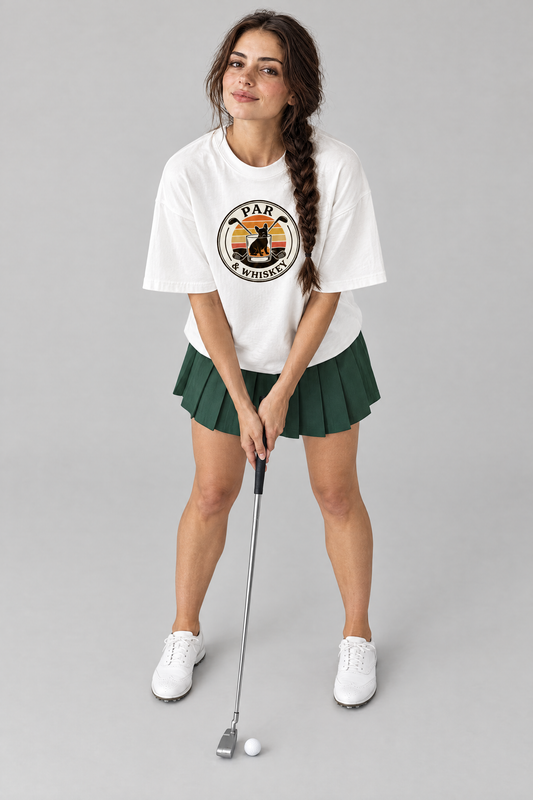 Woman lining up a putt in the white Par & Whiskey French Bulldog Badge Golf Tee and a green pleated skirt. Color: White
