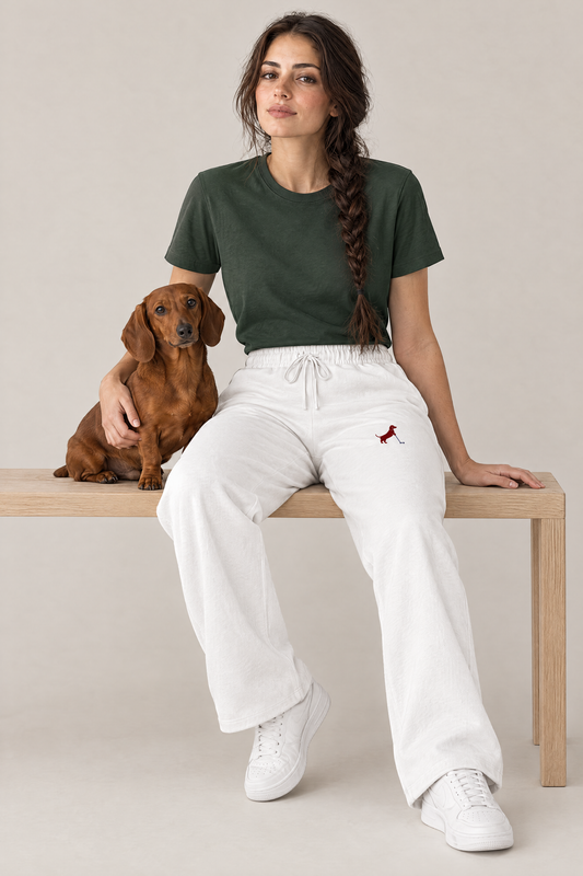 Woman sitting on a wooden bench with a red dachshund in white Putting dachshund golf sweatpants and a dark green tee. Color: White