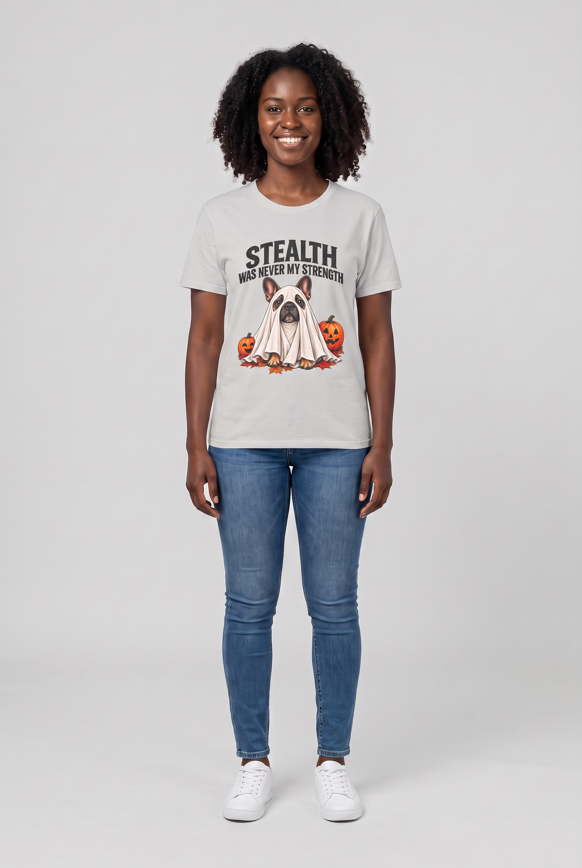 Woman wearing an ice grey French bulldog Halloween t-shirt with a Frenchie ghost and the text Stealth Was Never My Strength, front view