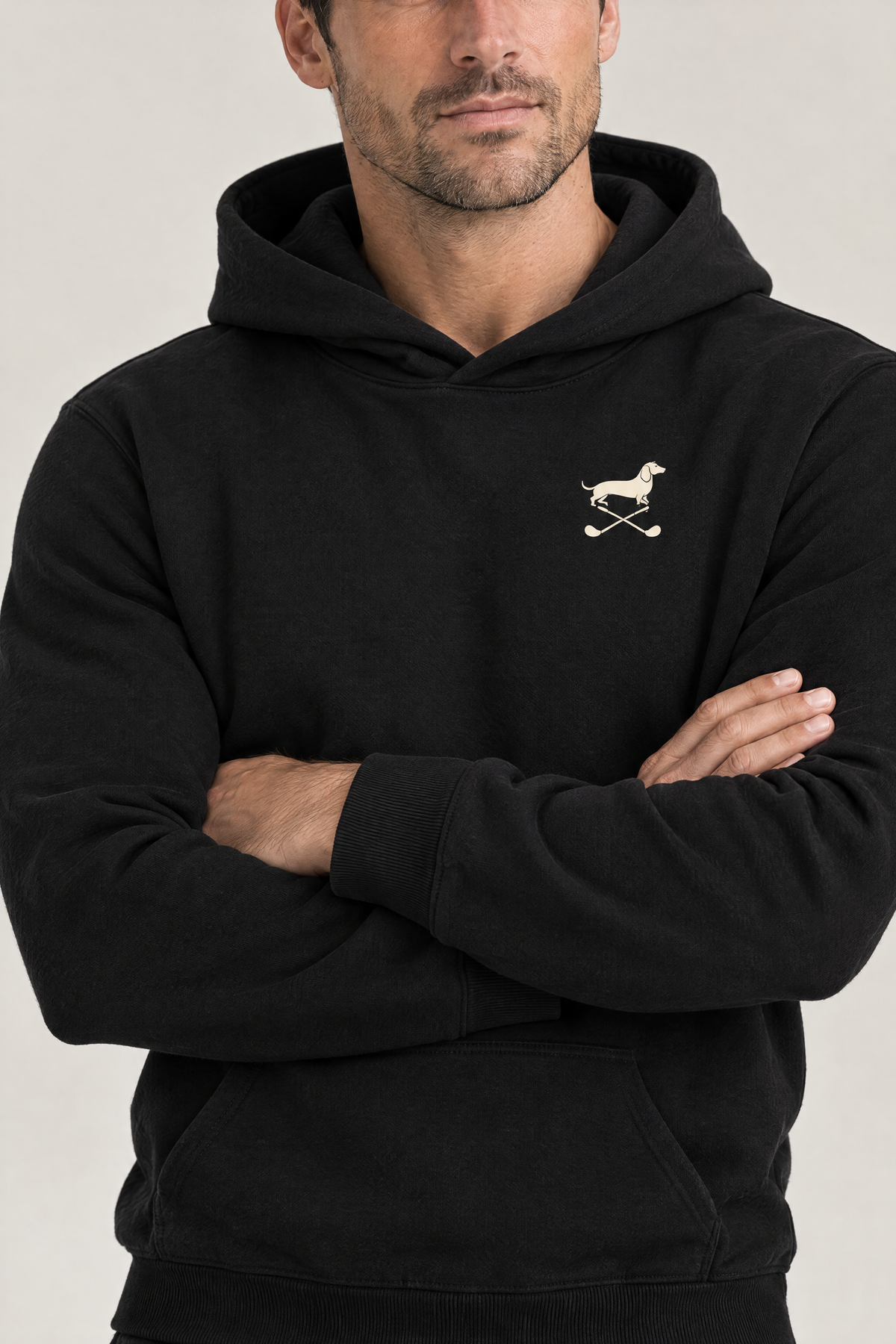 Close-up of man with crossed arms wearing black Club & Swing dachshund golf hoodie, chest print detail. Color: Black