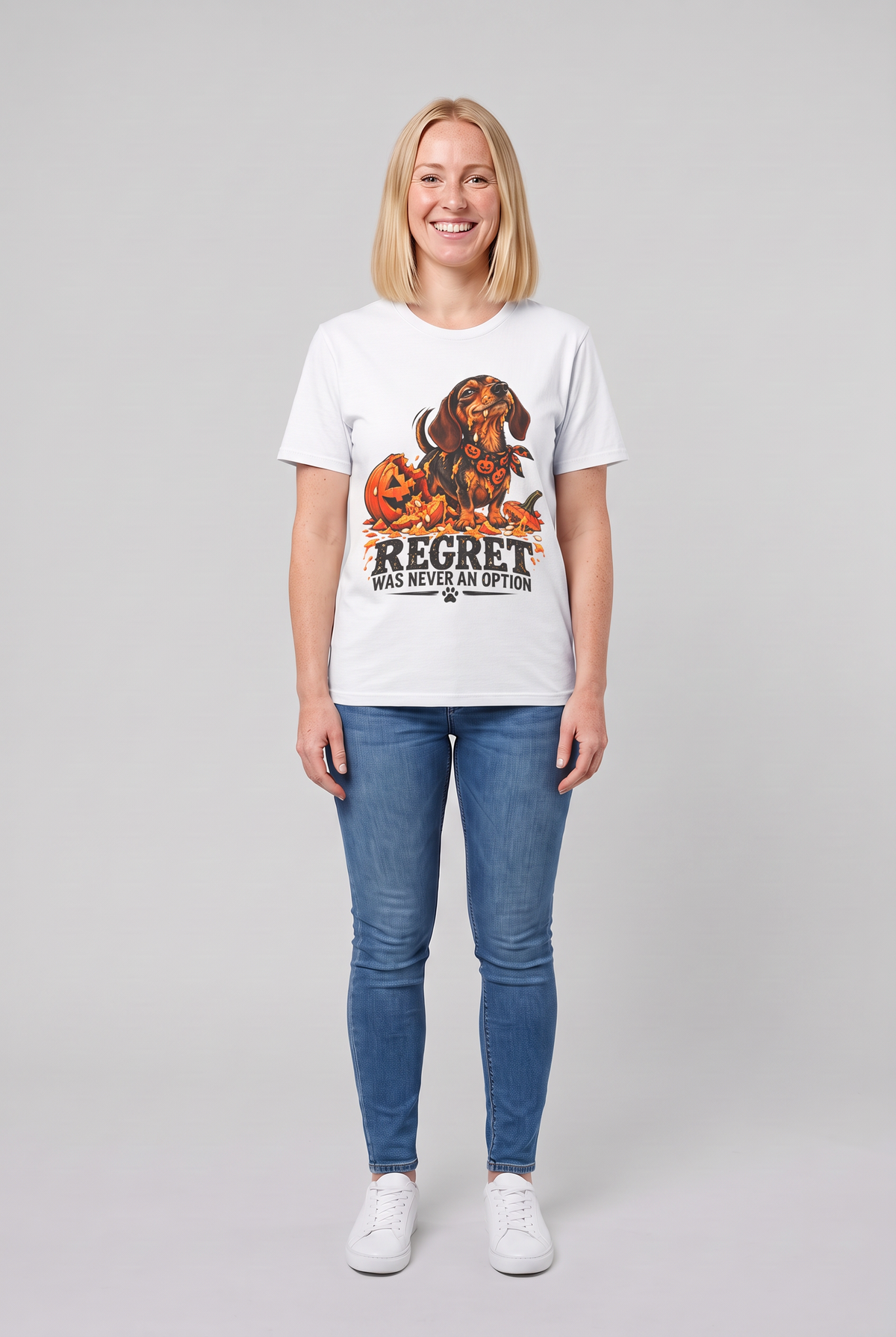 Woman wearing a white funny dachshund Halloween t-shirt with a wiener dog next to a smashed jack-o-lantern and the text Regret Was Never An Option, front view