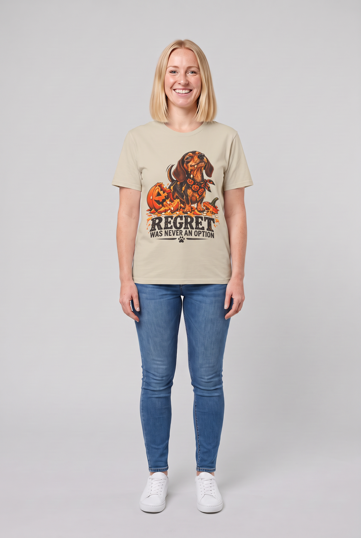 Woman wearing a sand funny dachshund Halloween t-shirt with a wiener dog next to a smashed jack-o-lantern and the text Regret Was Never An Option, front view