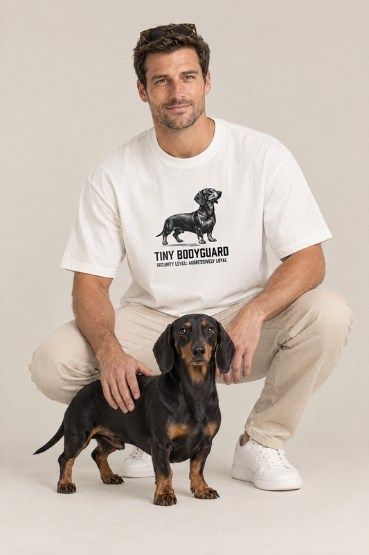 Man crouching with a black and tan dachshund in the white Tiny Bodyguard Dachshund Tee. Color: White
