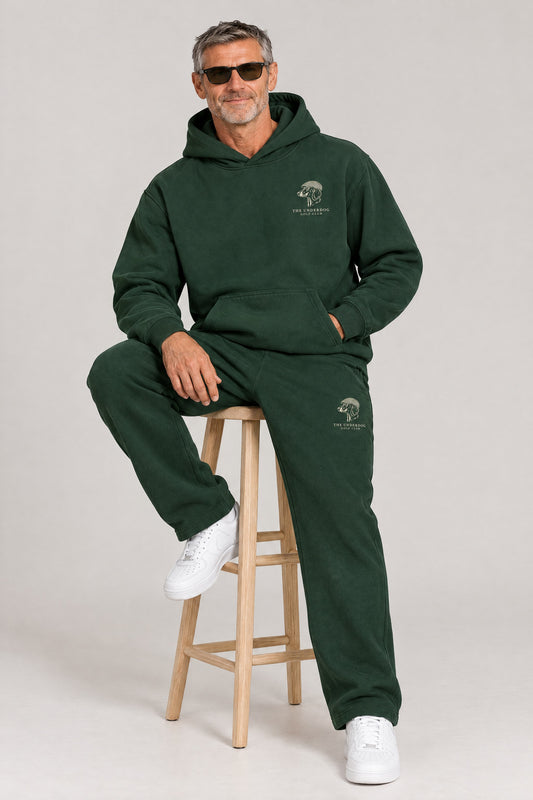 Man seated in The Long Drive dachshund golf hoodie and sweatpants in Blackish Green. Color: Blackish Green