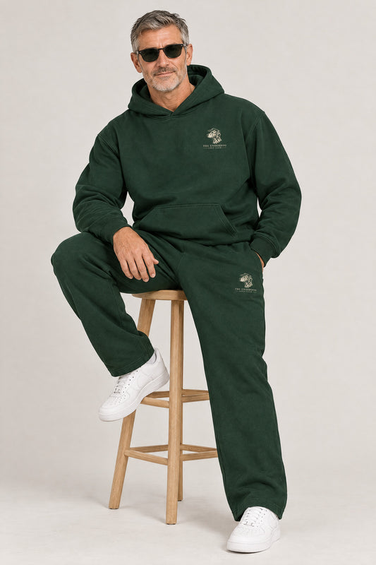 Man seated in The Sweet Spot Dalmatian golf hoodie and sweatpants in Blackish Green. Color: Blackish Green