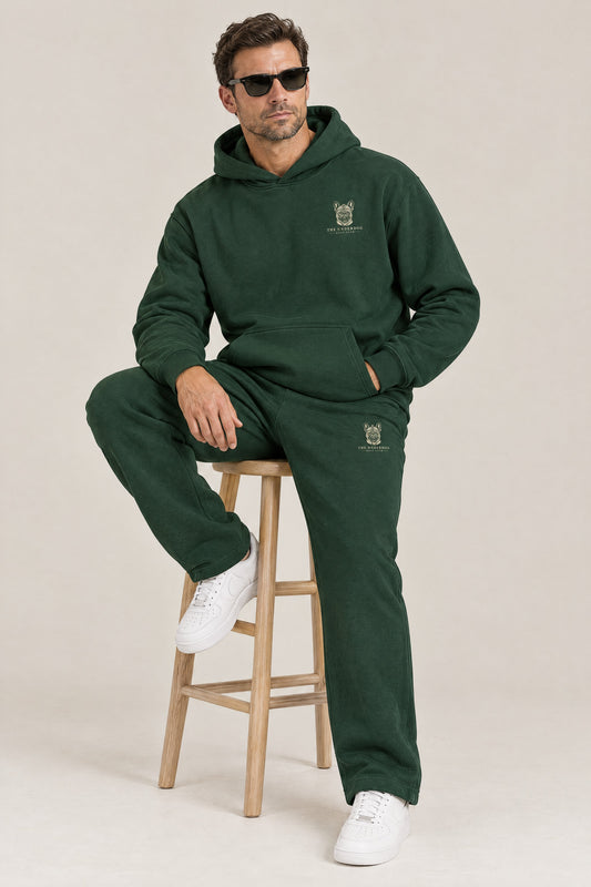 Man seated in The Marshal French Bulldog golf hoodie and sweatpants in Blackish Green. Color: Blackish Green