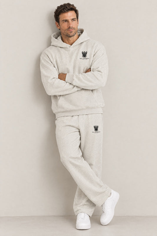 Man seated in The Marshal French Bulldog golf hoodie and sweatpants in Oat Gray. Color: Oat Gray