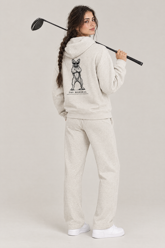 Woman with a driver over her shoulder, back view of The Marshal French Bulldog golf hoodie in Oat Gray with the large back print. Color: Oat Gray