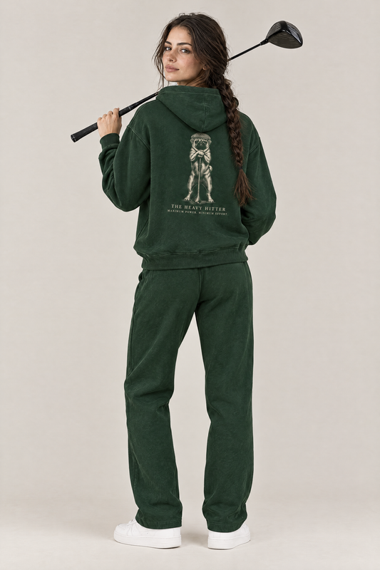 Woman with a driver over her shoulder, back view of The Heavy Hitter pug golf hoodie in Blackish Green with the large back print. Color: Blackish Green