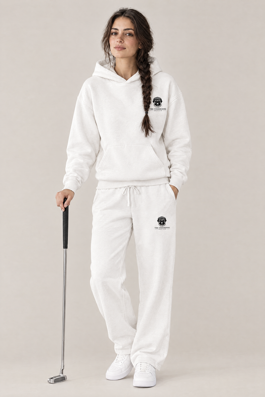 Woman holding a putter in The Heavy Hitter pug golf hoodie and matching Underdog Golf Club sweatpants in White, front view. Color: White
