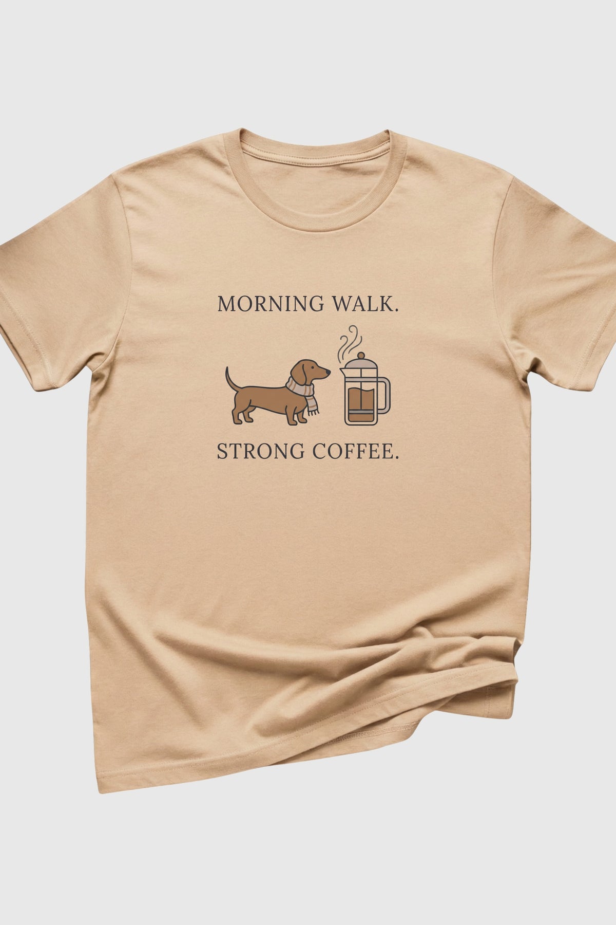 Beige t-shirt with a graphic of a dachshund and coffee cup, text 'Morning Walk. Strong Coffee.' on a white background.