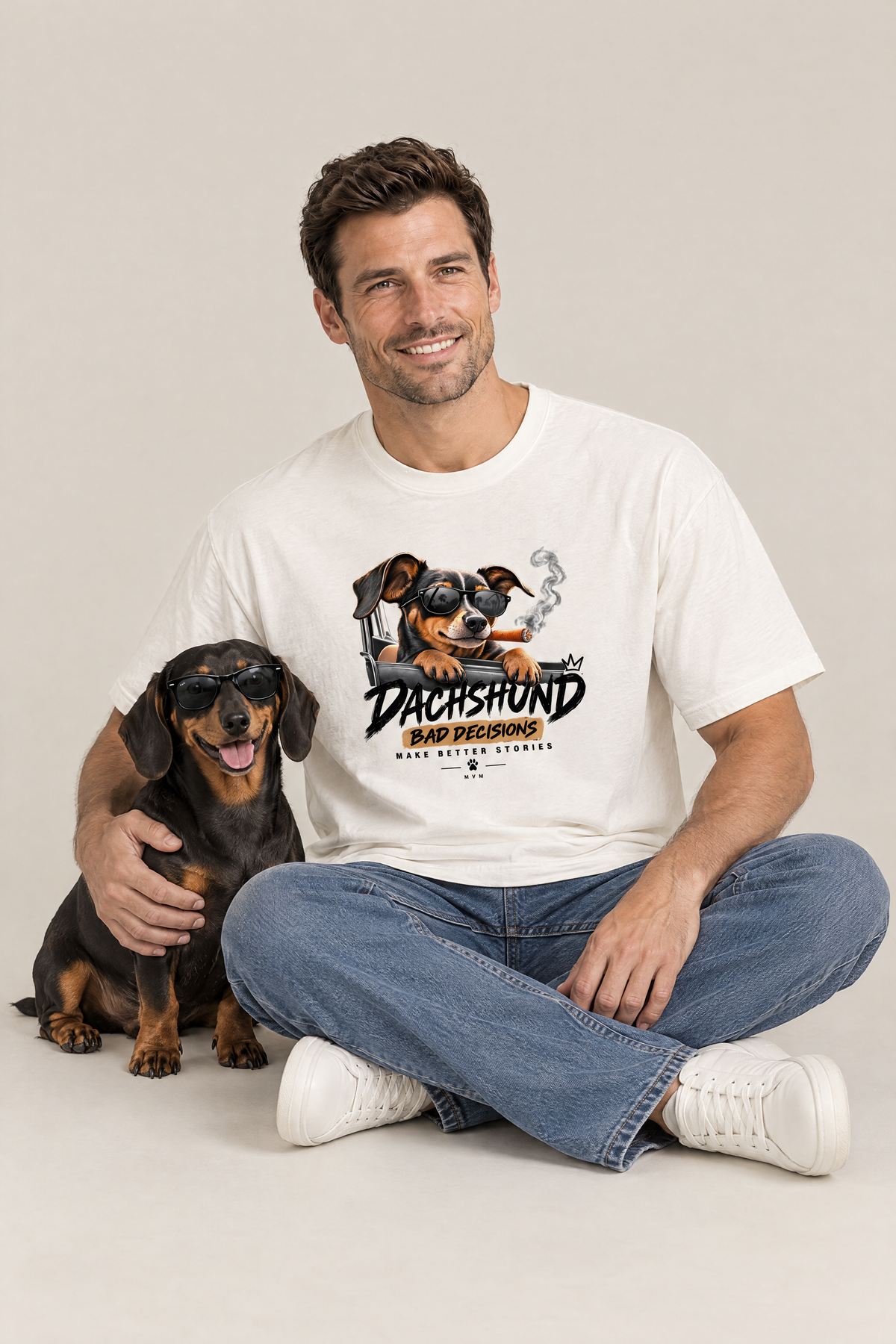 Man sitting on the floor with a black and tan dachshund in sunglasses in the white Bad Decisions Dachshund Tee. Color: White
