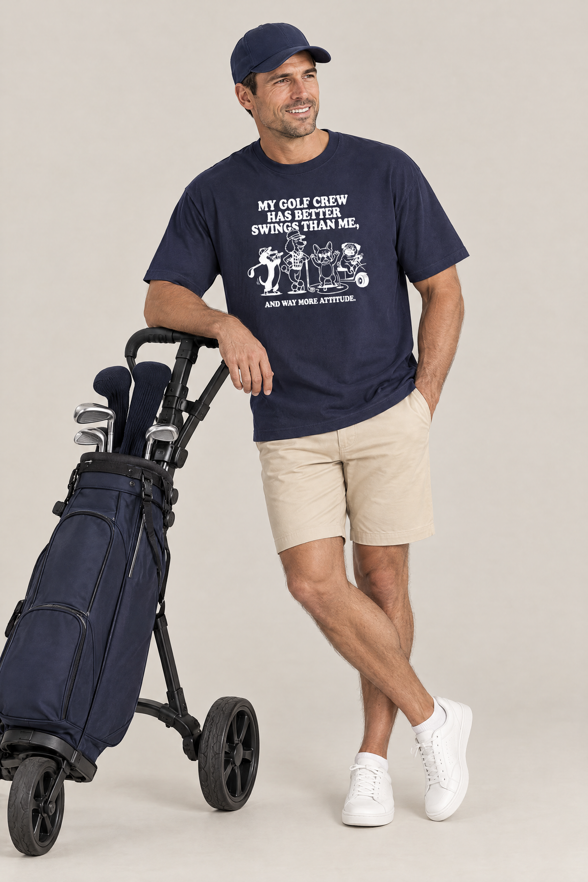 Man leaning on a golf push trolley in the navy Better Swings Dog Golf Tee. Color: Navy