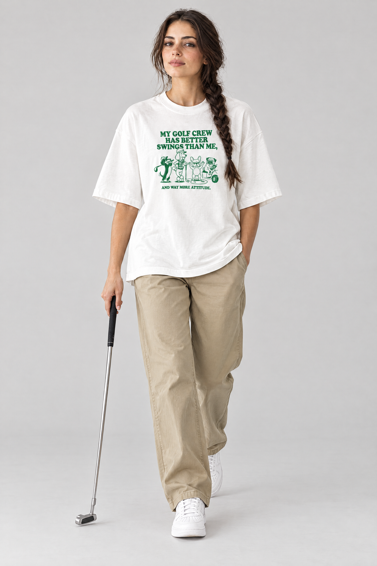 Woman walking with a putter in the white Better Swings Dog Golf Tee and khaki trousers. Color: White