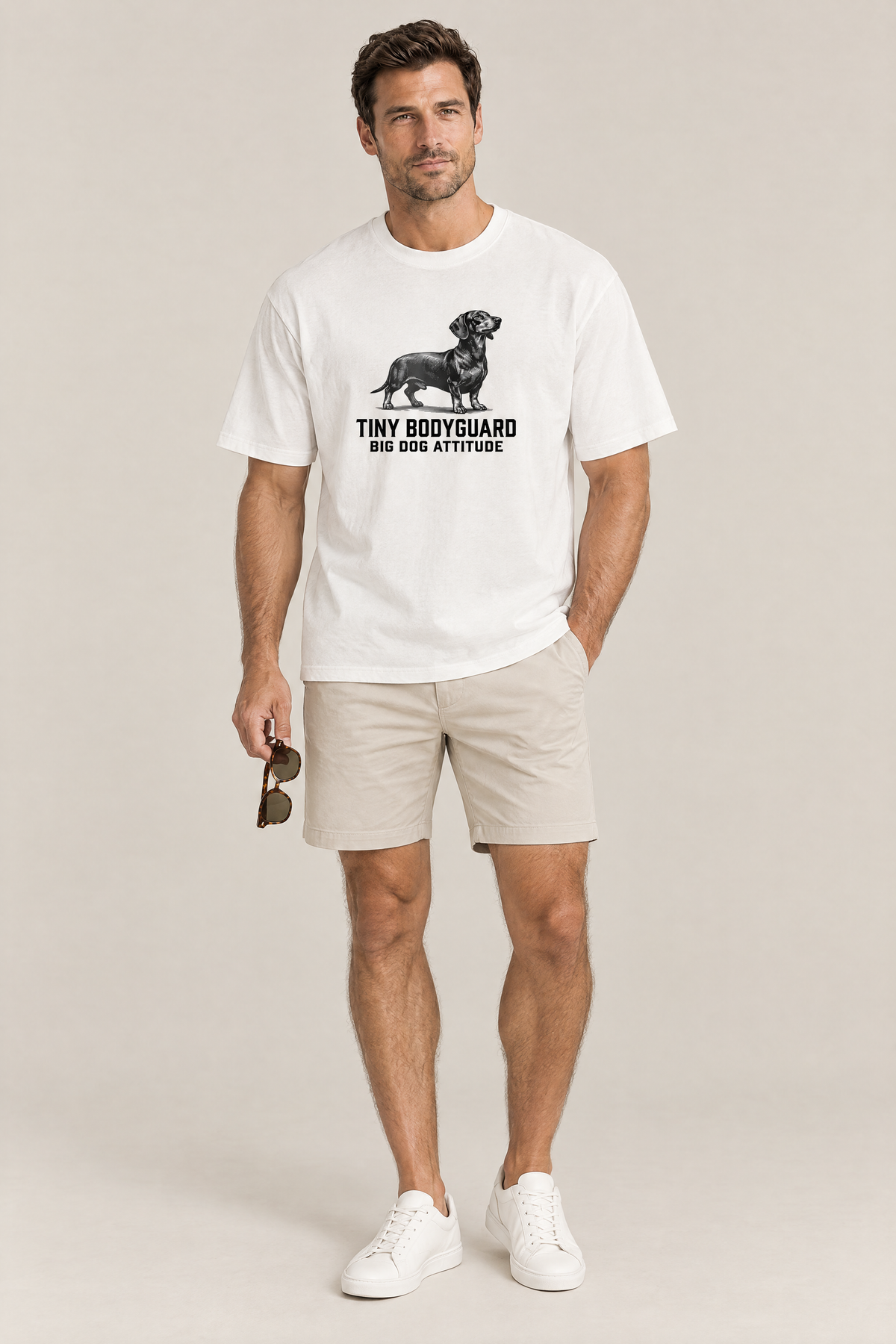 Man wearing the Big Dog Attitude Dachshund Tee in white with beige shorts and white sneakers. Color: White