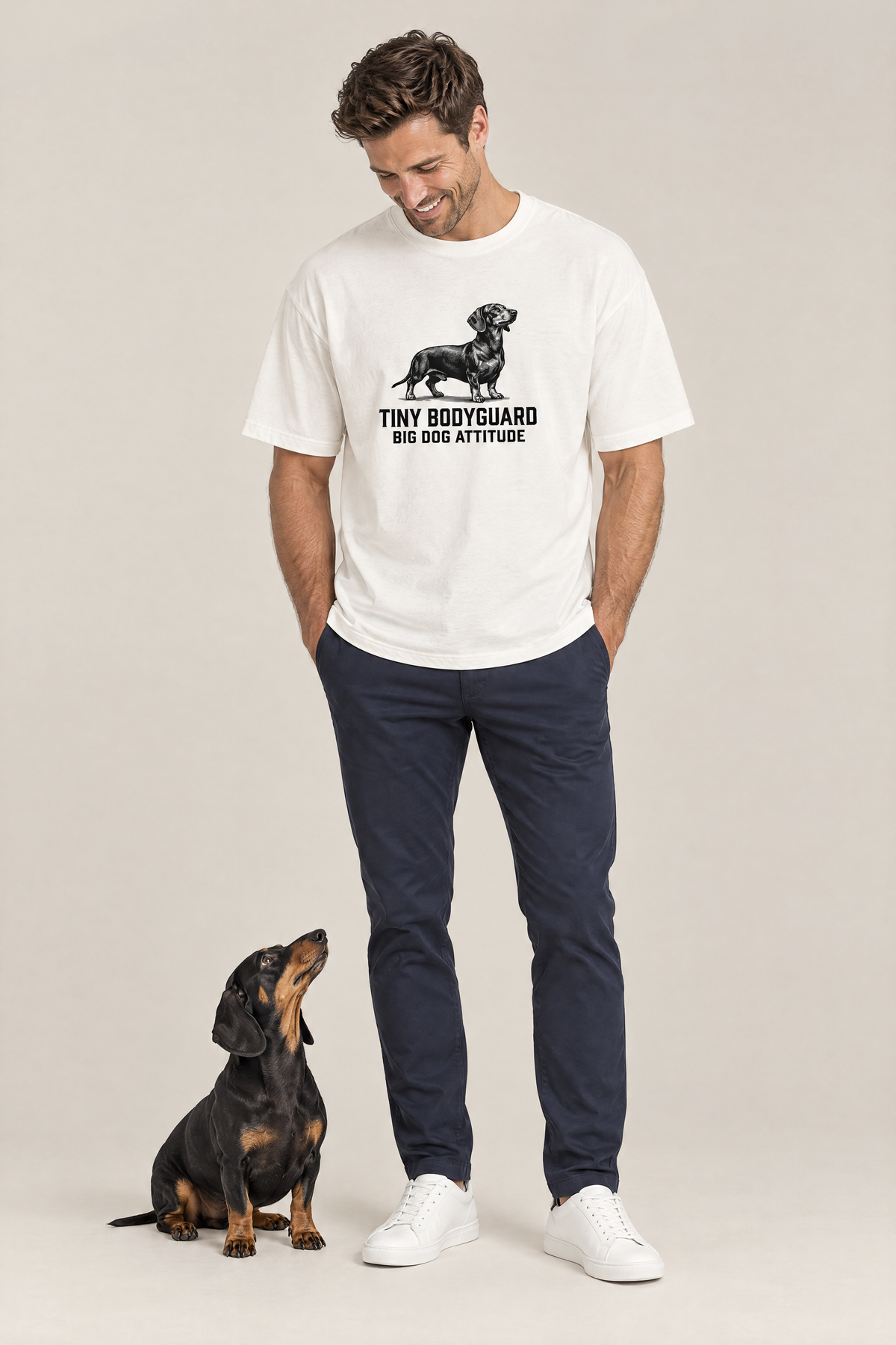 Man smiling at a black and tan dachshund sitting at his feet in the white Big Dog Attitude Dachshund Tee. Color: White