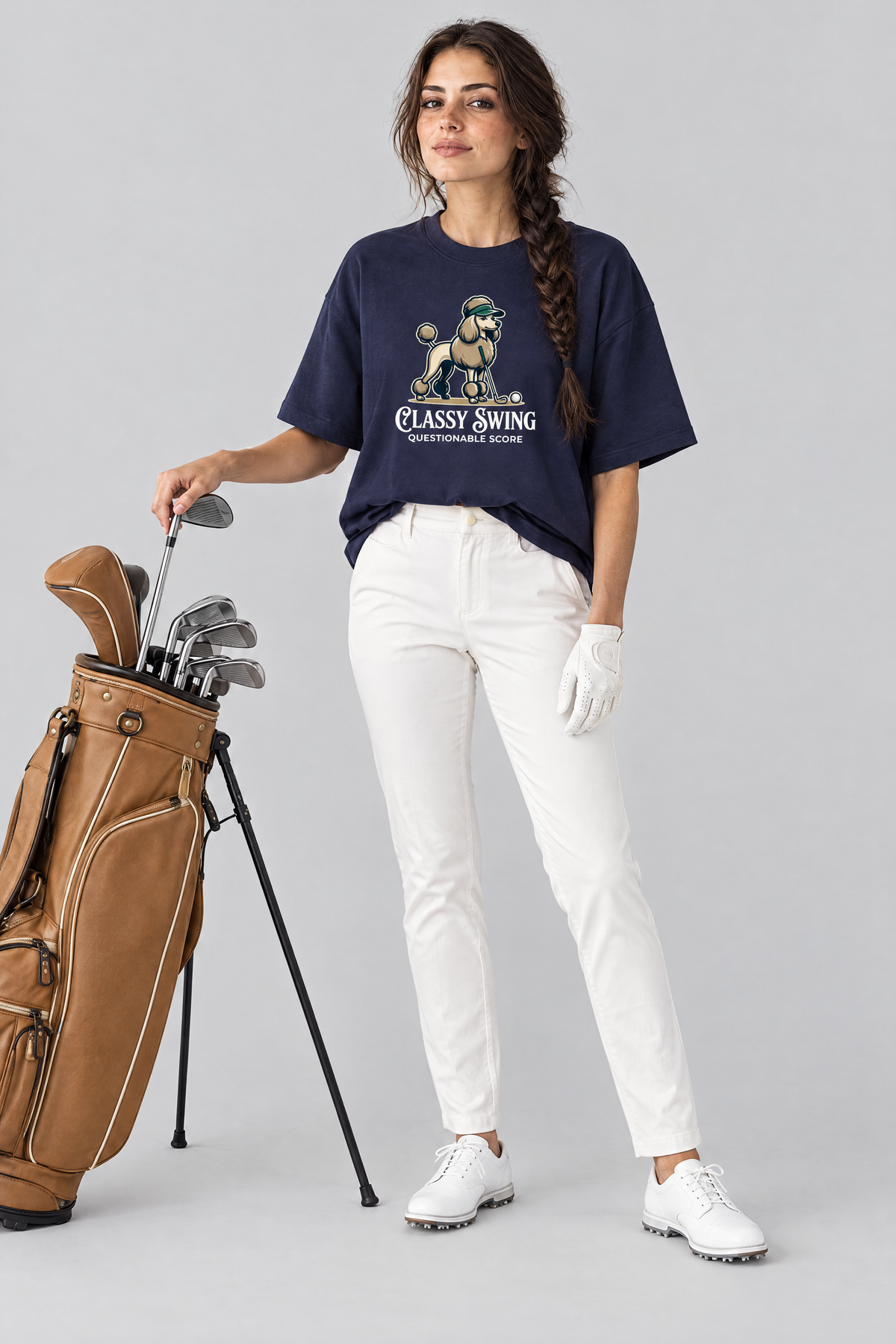 Woman pulling an iron from a tan golf bag, wearing the Classy Swing Poodle Golf Tee with white golf trousers. Color: Navy