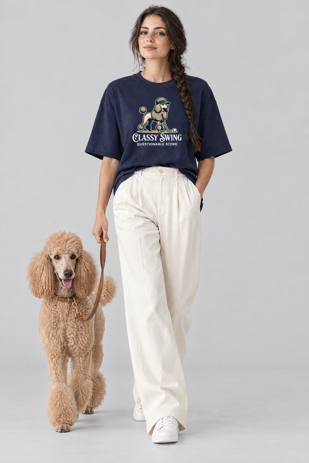 Woman walking an apricot standard poodle on a leash, wearing the Classy Swing Poodle Golf Tee. Color: Navy