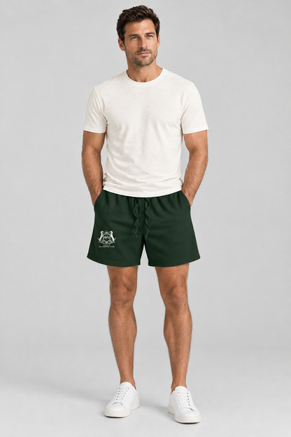 Man in blackish green Club Crest shorts with the small cream crest on the leg and a white tee, full body. Color: Blackish Green