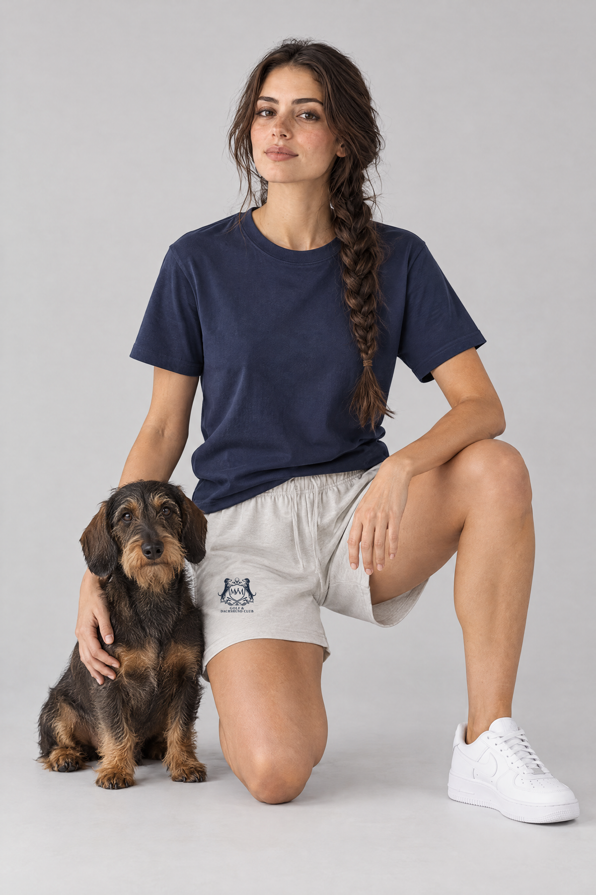 Woman kneeling next to a wire-haired dachshund in oat gray Club Crest shorts and a navy tee. Color: Oat Gray
