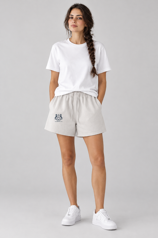 Woman in oat gray Club Crest shorts with the small navy Golf & Dachshund Club crest and a white tee, full body. Color: Oat Gray