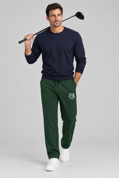 Man walking with a driver over his shoulder in blackish green Club Crest sweatpants and a navy sweater. Color: Blackish Green