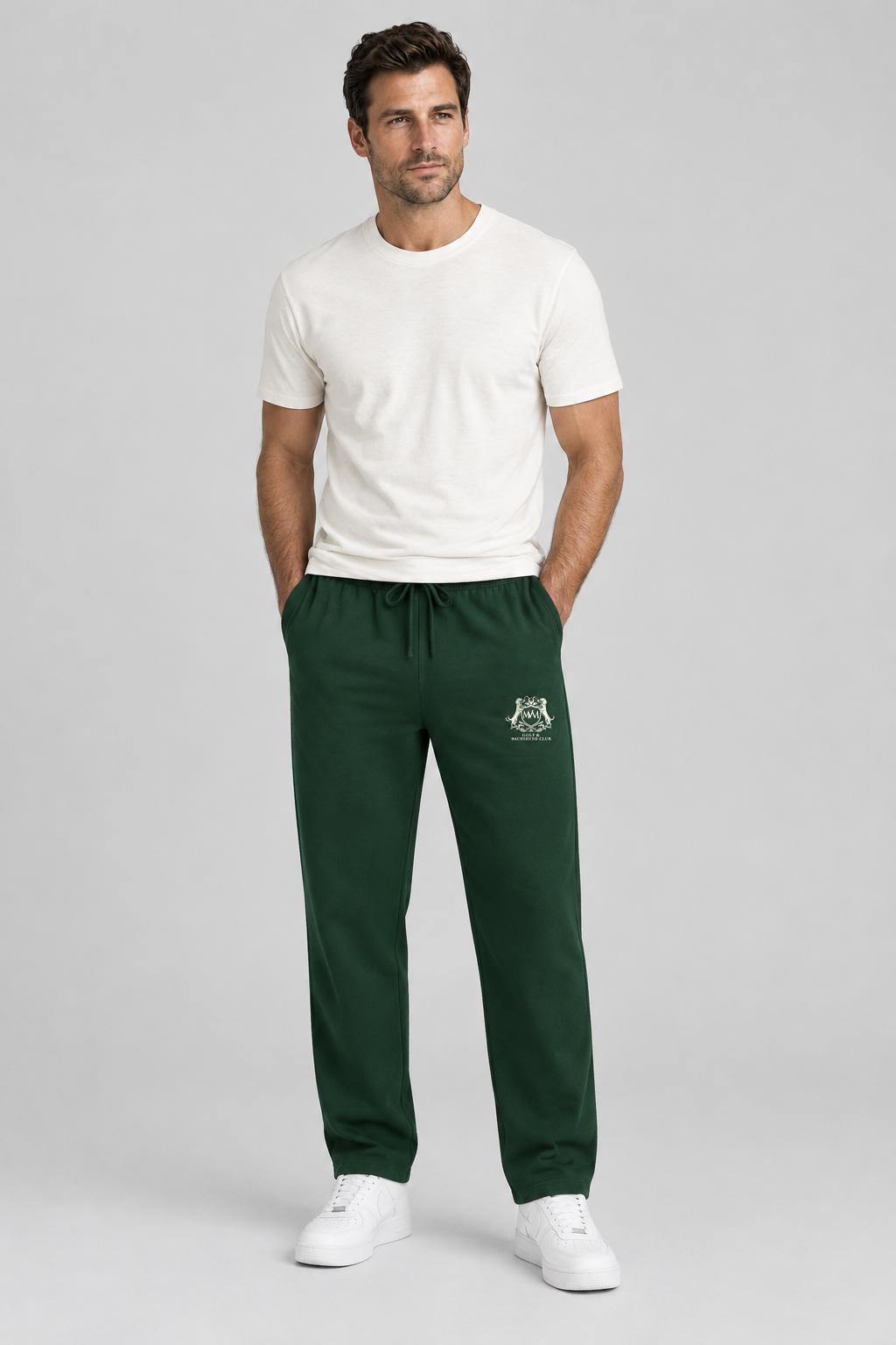 Man in blackish green straight-leg Club Crest sweatpants with the small cream crest on the thigh and a white tee, full body. Color: Blackish Green