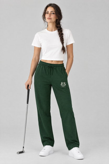 Woman holding a putter in blackish green Club Crest sweatpants with the small cream Golf & Dachshund Club crest on the thigh and a white cropped tee. Color: Blackish Green
