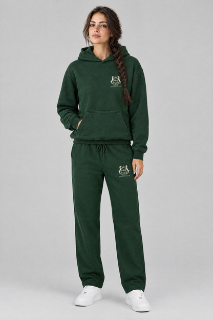 Woman in a matching blackish green set of Club Crest hoodie and sweatpants, both with the small cream crest. Color: Blackish Green