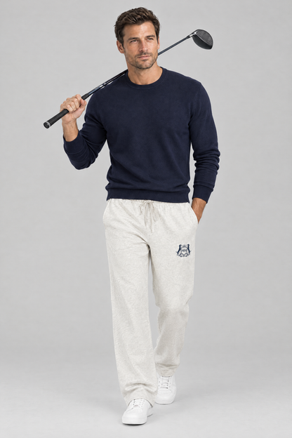 Man walking with a driver over his shoulder in oat gray Club Crest sweatpants and a navy sweater. Color: Oat Gray