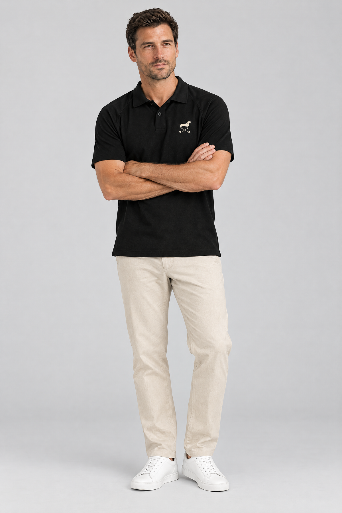 Man with crossed arms in the black Club Mark dachshund golf polo and light beige trousers. Color: Black