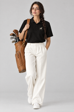 Woman carrying a tan leather golf bag in the black Club Mark dachshund golf polo and white wide-leg trousers. Color: Black