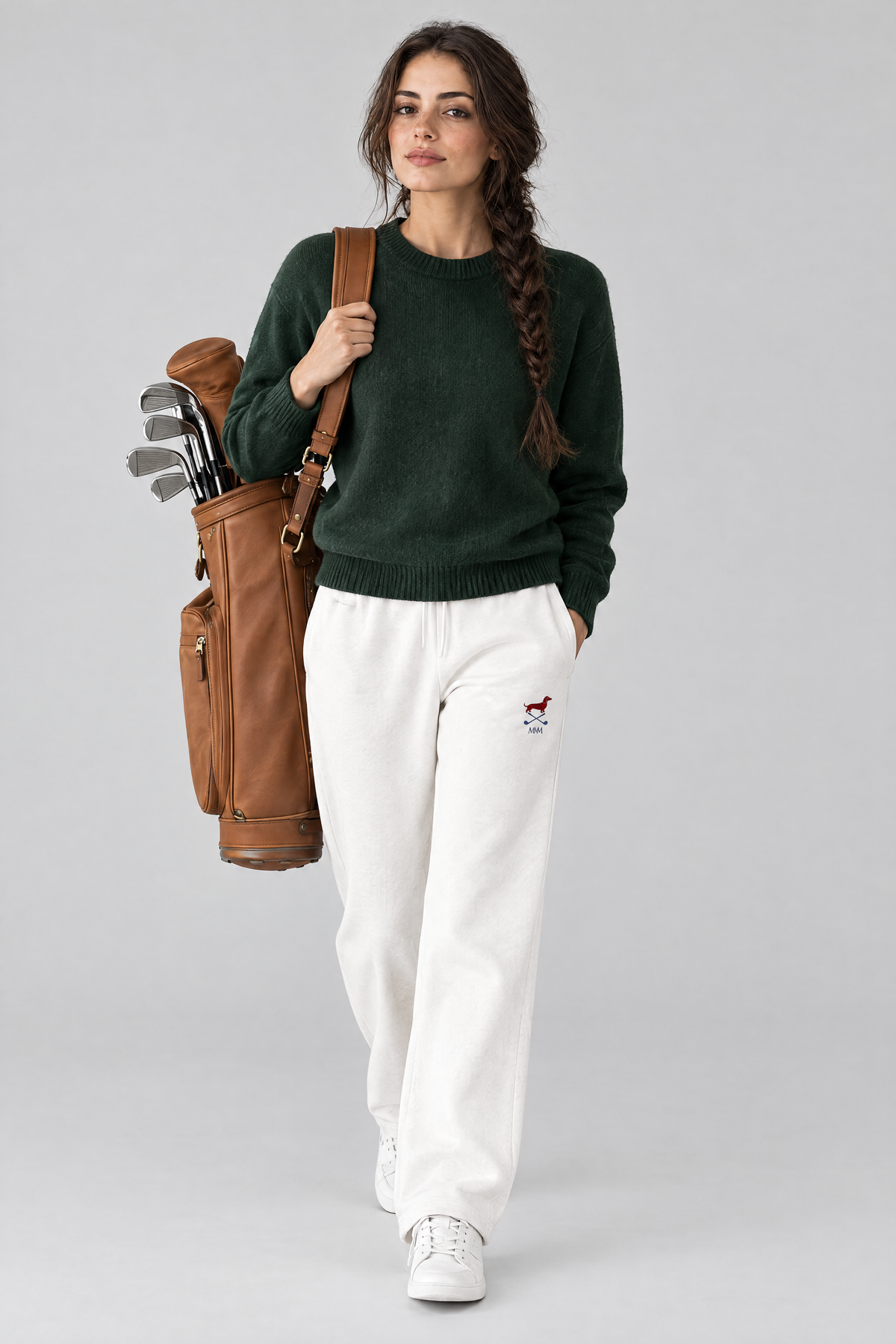 Woman walking with a tan leather golf bag in white Club Mark dachshund golf sweatpants and a dark green knit sweater. Color: White