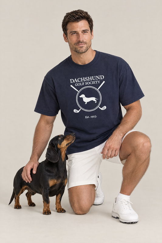 Man kneeling next to a black and tan dachshund in the navy Dachshund Golf Society Tee. Color: Navy