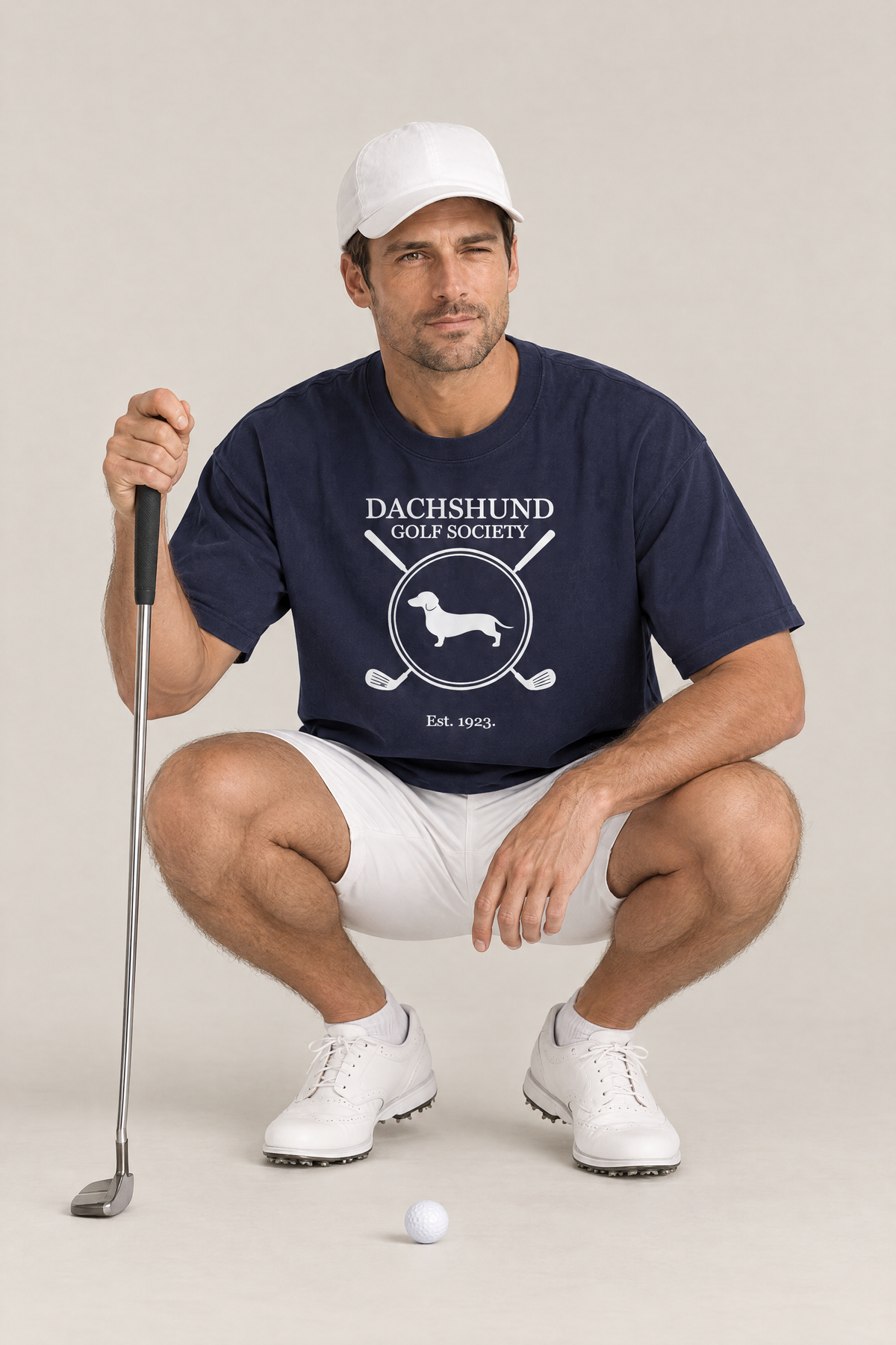 Man reading the green with a putter in the navy Dachshund Golf Society Tee. Color: Navy