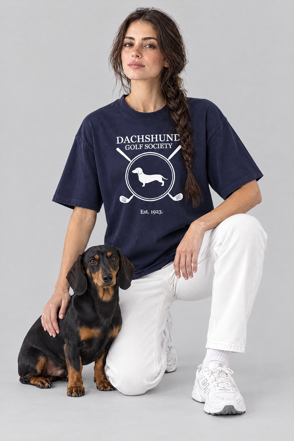 Woman kneeling next to a black and tan dachshund in the navy Dachshund Golf Society Tee. Color: Navy