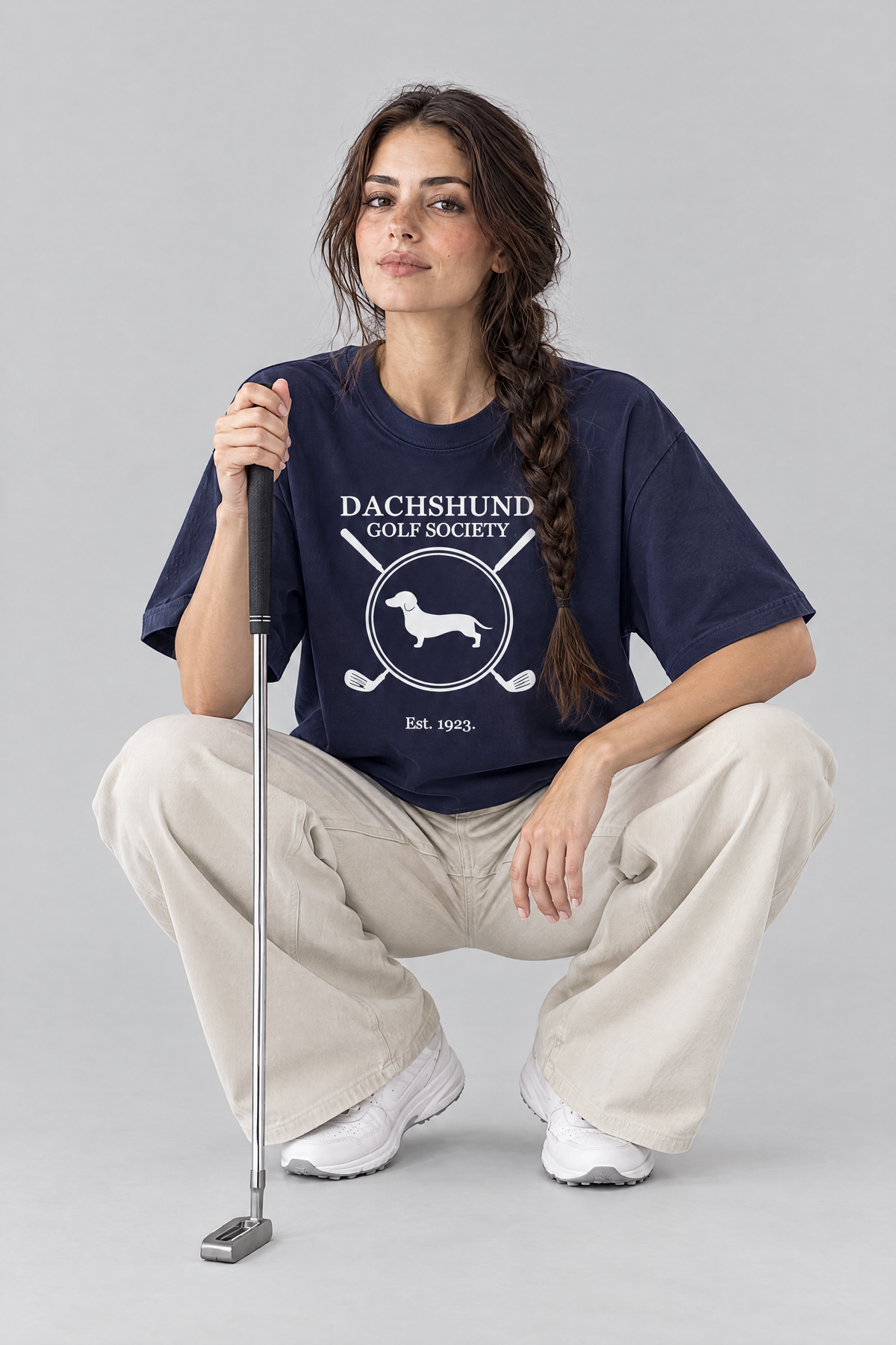 Woman crouching to read the green with a putter in the navy Dachshund Golf Society Tee. Color: Navy