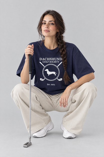 Woman crouching to read the green with a putter in the navy Dachshund Golf Society Tee. Color: Navy