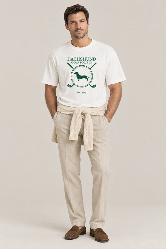 Man wearing the Dachshund Golf Society Tee in white with stone trousers and a sweater tied around his hips. Color: White