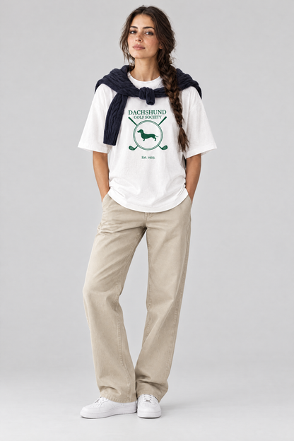 Woman wearing the Dachshund Golf Society Tee in white with stone trousers and a navy sweater over her shoulders. Color: White